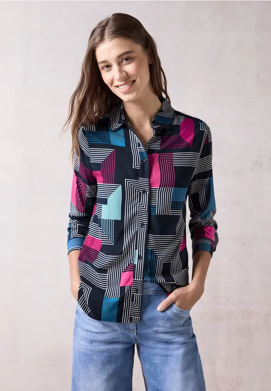 Une femme porte une chemise Cecil à motifs graphiques colorés sur un jean clair.