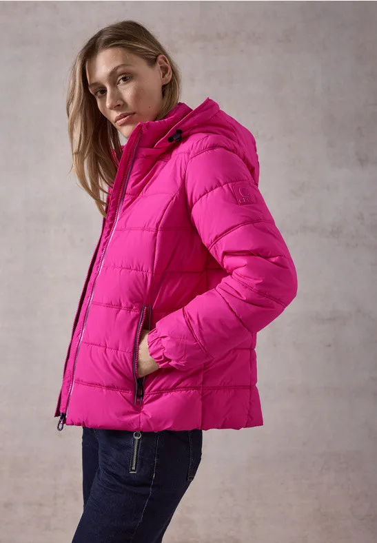Une femme porte une doudoune fuchsia à capuche sur un jean foncé.