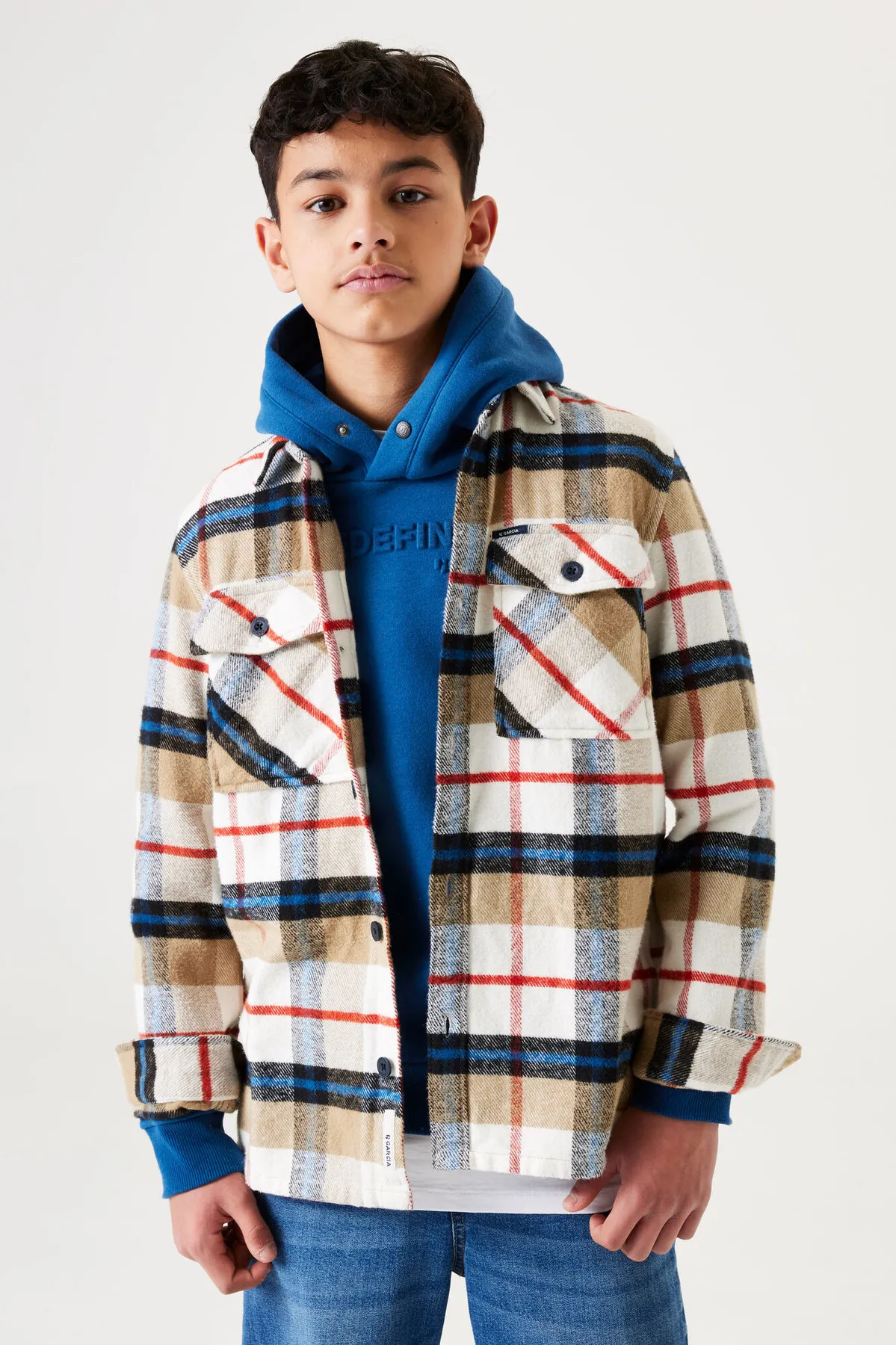 Un garçon porte une surchemise à carreaux beige sur un sweat à capuche bleu.