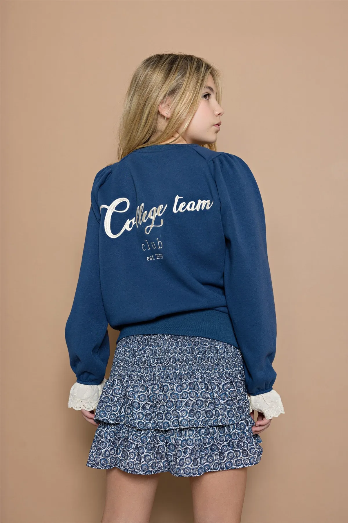 Une adolescente porte un sweat bleu et une jupe imprimée de la collection enfants.