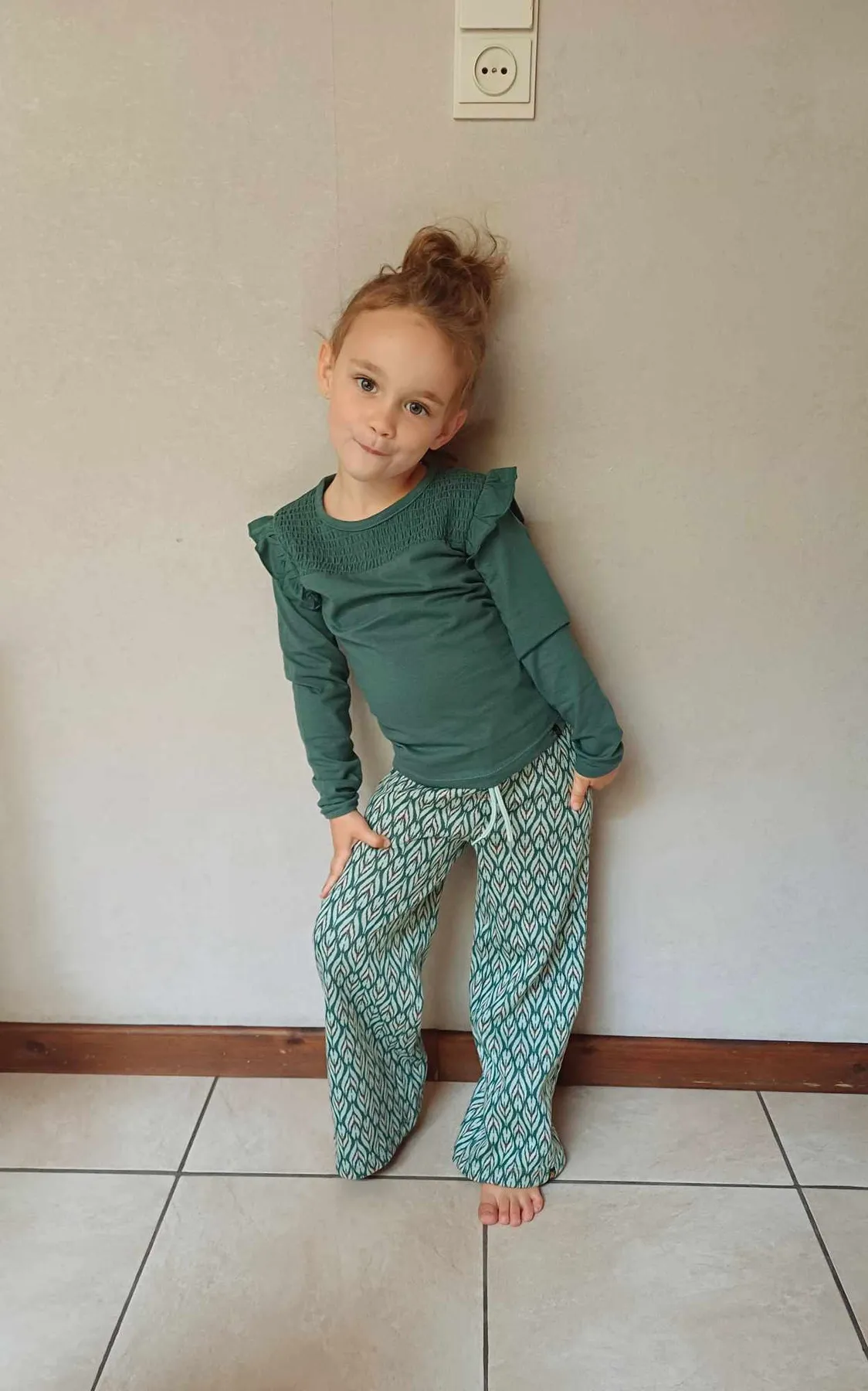 Une petite fille porte un haut vert à volants et un pantalon large assorti.