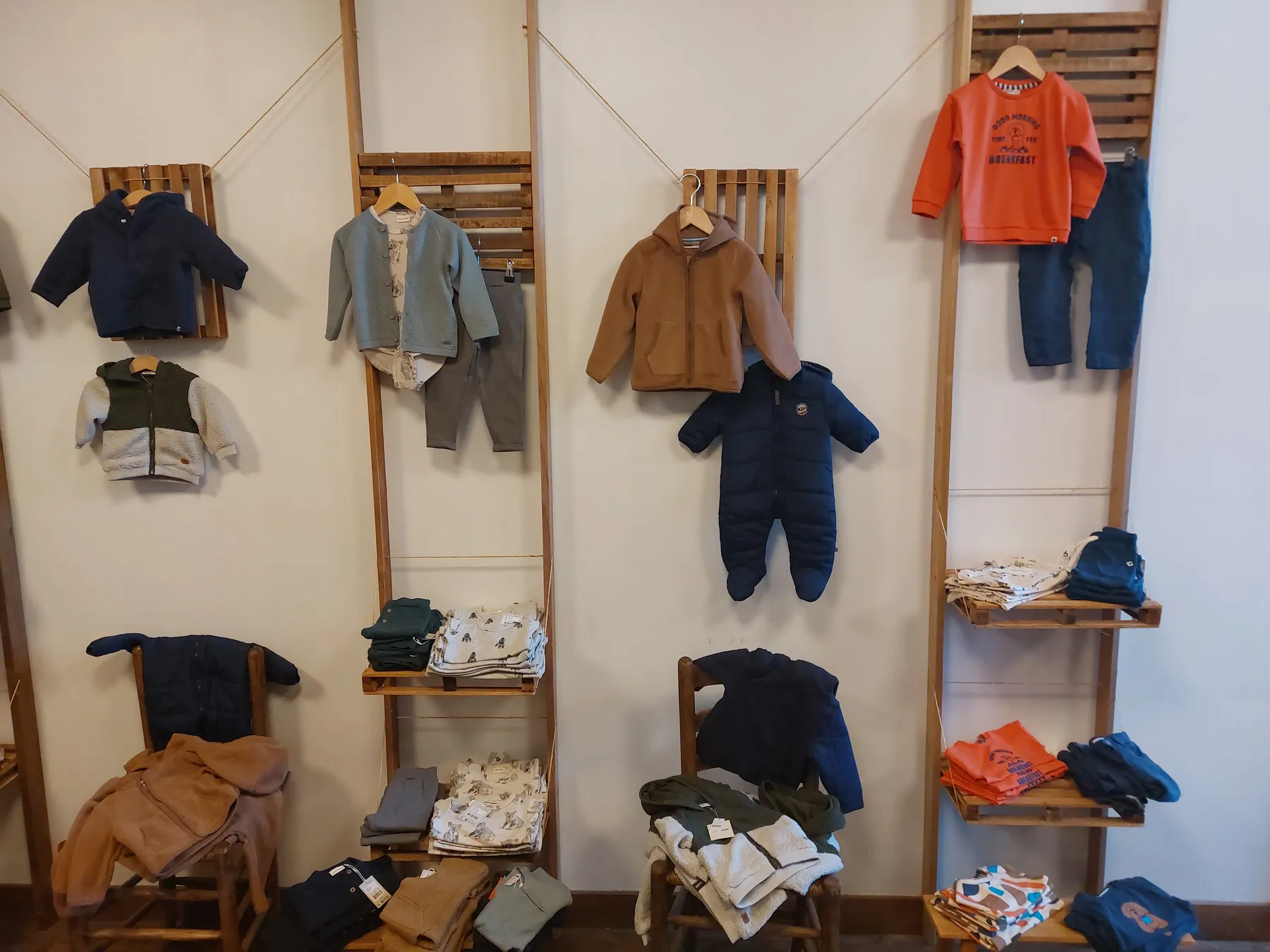 Un mur de la boutique où sont suspendues des tenues pour bébés sur des cintres en bois.